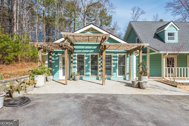 rear view of property with a shingled roof and a pergola