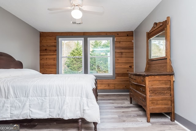 bedroom featuring visible vents, a ceiling fan, wood walls, wood finished floors, and baseboards