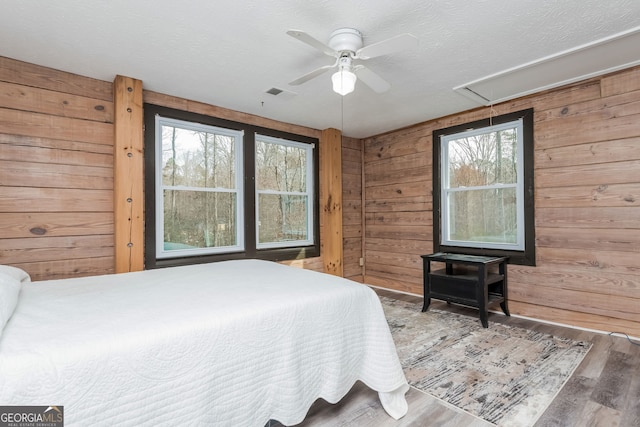 bedroom featuring attic access, visible vents, wooden walls, and wood finished floors