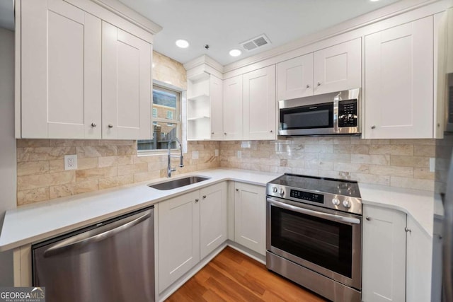 kitchen with appliances with stainless steel finishes, sink, white cabinets, and backsplash