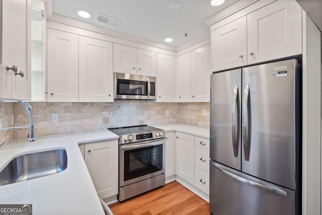 kitchen with appliances with stainless steel finishes, sink, white cabinets, and light hardwood / wood-style floors