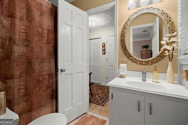 bathroom featuring vanity, ornamental molding, toilet, tile patterned floors, and a textured ceiling