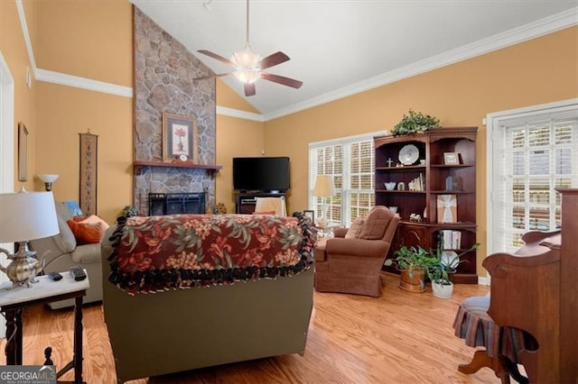 living room with crown molding, a stone fireplace, a wealth of natural light, and light hardwood / wood-style flooring