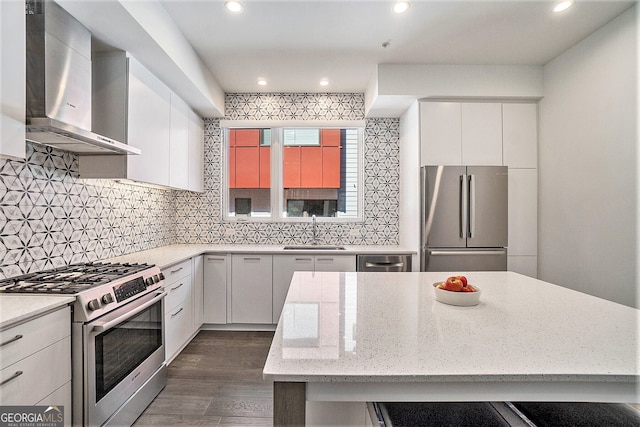 kitchen with appliances with stainless steel finishes, sink, white cabinets, light stone countertops, and wall chimney range hood