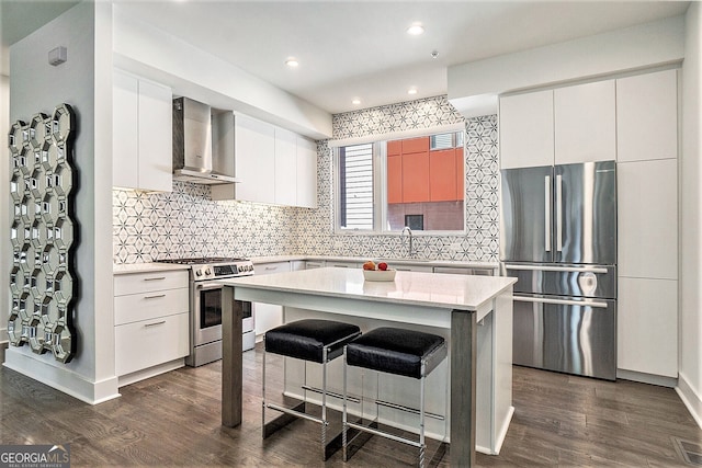 kitchen featuring wall chimney range hood, stainless steel appliances, a center island, white cabinets, and a kitchen bar