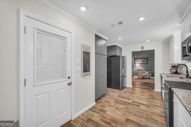 kitchen with appliances with stainless steel finishes, sink, crown molding, a textured ceiling, and light hardwood / wood-style flooring