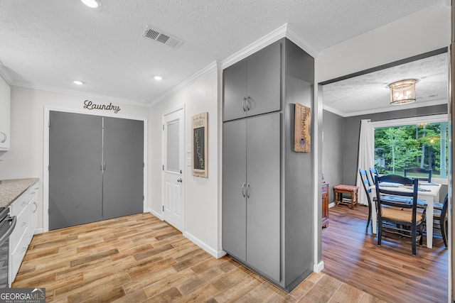 kitchen featuring white cabinetry, ornamental molding, light hardwood / wood-style floors, stainless steel range oven, and a textured ceiling