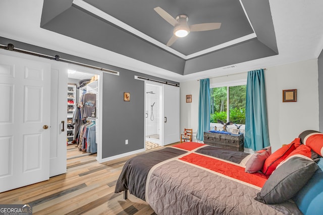 bedroom featuring wood-type flooring, a raised ceiling, a barn door, a spacious closet, and a closet