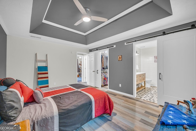 bedroom with hardwood / wood-style floors, ceiling fan, a tray ceiling, a barn door, and ensuite bath