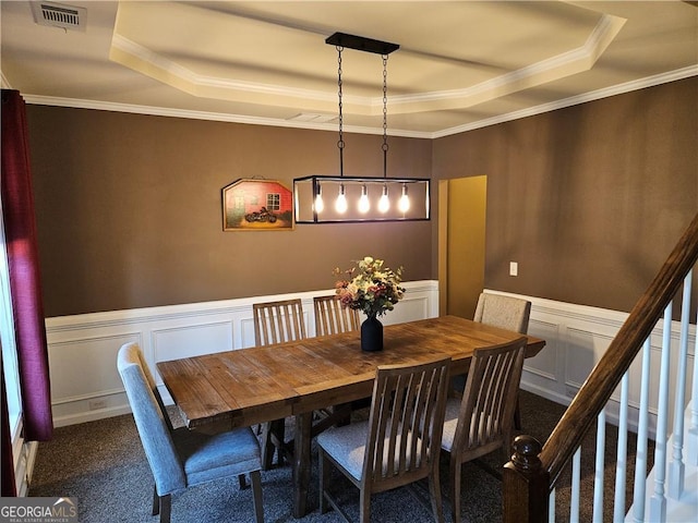 carpeted dining room with visible vents, a tray ceiling, and a wainscoted wall