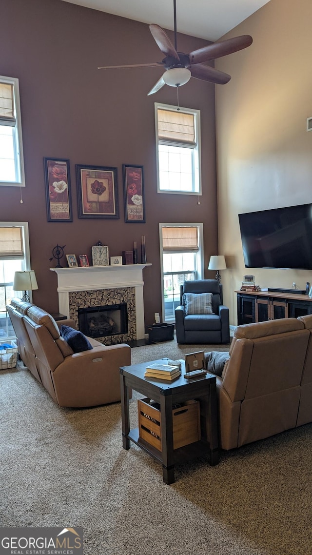 carpeted living area featuring a tiled fireplace, a high ceiling, and ceiling fan