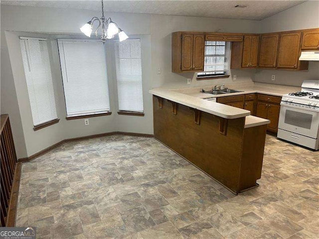 kitchen featuring kitchen peninsula, decorative light fixtures, sink, a kitchen breakfast bar, and gas range gas stove