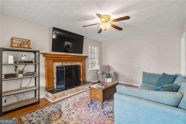 living room featuring ceiling fan, hardwood / wood-style floors, a tile fireplace, and a textured ceiling