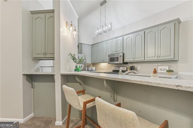 kitchen featuring appliances with stainless steel finishes, pendant lighting, a kitchen bar, carpet, and light stone counters