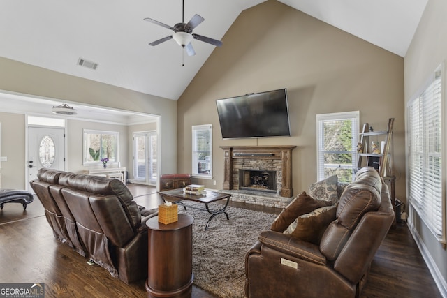 living room featuring dark hardwood / wood-style flooring, a stone fireplace, high vaulted ceiling, and ceiling fan