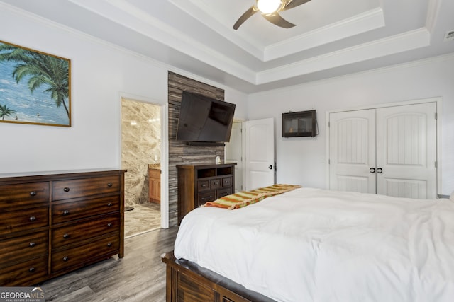 bedroom featuring ceiling fan, a tray ceiling, crown molding, light wood-type flooring, and a closet