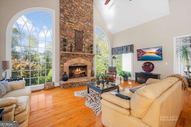 living room featuring hardwood / wood-style flooring, ceiling fan, a fireplace, and high vaulted ceiling