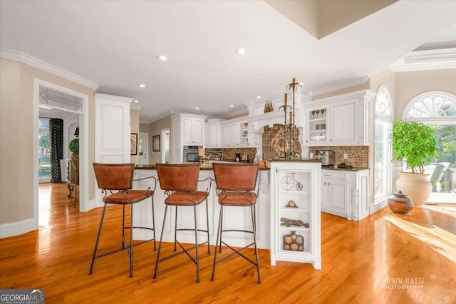 kitchen with a breakfast bar area, white cabinetry, tasteful backsplash, light wood-type flooring, and a kitchen island