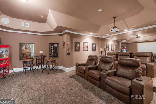 cinema with ornamental molding, a raised ceiling, and carpet flooring