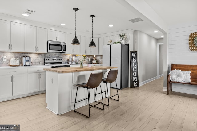 kitchen with stainless steel appliances, a center island, wooden counters, and white cabinets