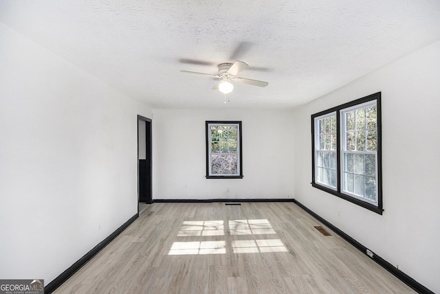 spare room with ceiling fan, plenty of natural light, a textured ceiling, and light wood-type flooring