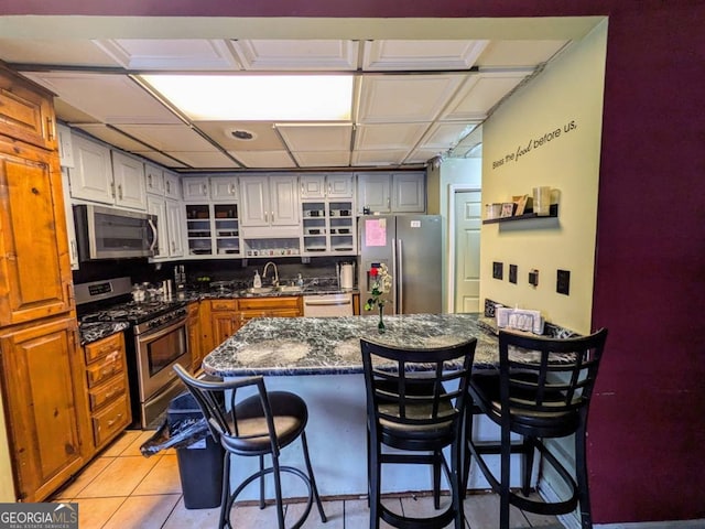 kitchen with white cabinetry, dark stone countertops, a kitchen bar, light tile patterned floors, and stainless steel appliances