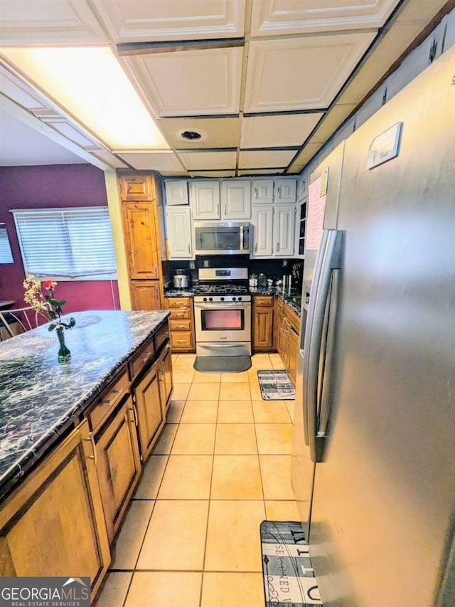 kitchen with stainless steel appliances, dark stone countertops, and light tile patterned floors