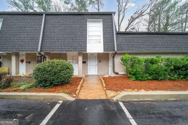 multi unit property featuring uncovered parking, mansard roof, roof with shingles, and brick siding