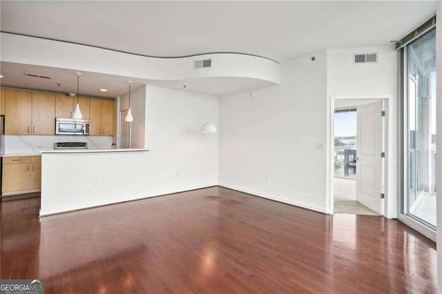 unfurnished living room featuring visible vents, dark wood-style flooring, and a healthy amount of sunlight
