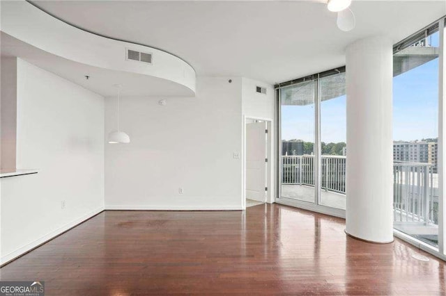 unfurnished room with visible vents, baseboards, wood finished floors, and a wall of windows