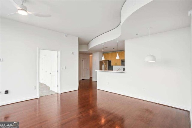 unfurnished living room with dark wood-type flooring, ceiling fan, and baseboards