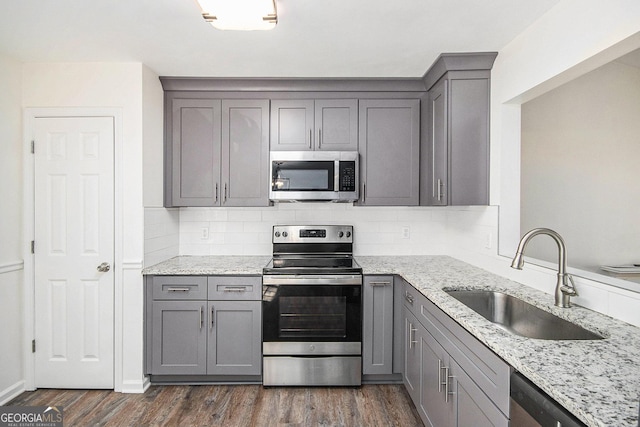 kitchen featuring appliances with stainless steel finishes, gray cabinets, a sink, and light stone counters