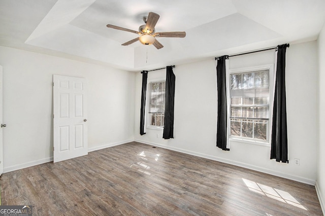 empty room with a raised ceiling, ceiling fan, baseboards, and wood finished floors