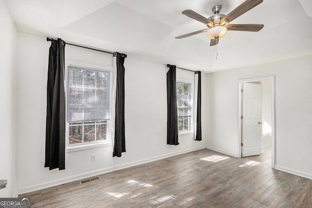 unfurnished room with dark wood-style floors, a ceiling fan, visible vents, and baseboards