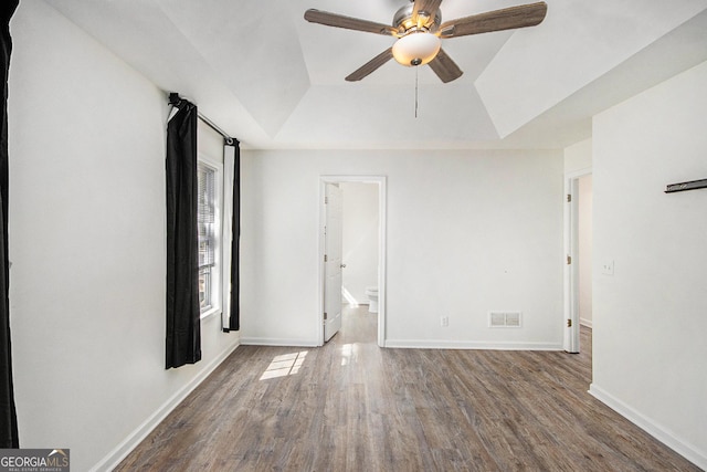 unfurnished bedroom featuring a raised ceiling, visible vents, dark wood-type flooring, ensuite bath, and baseboards