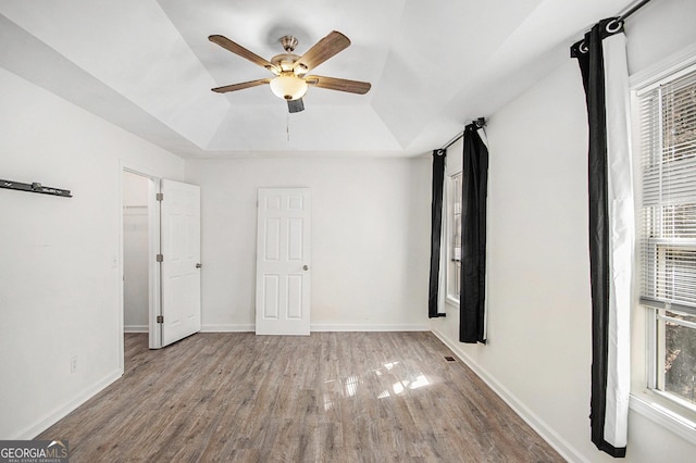 unfurnished bedroom featuring a tray ceiling, light wood-type flooring, a ceiling fan, and baseboards