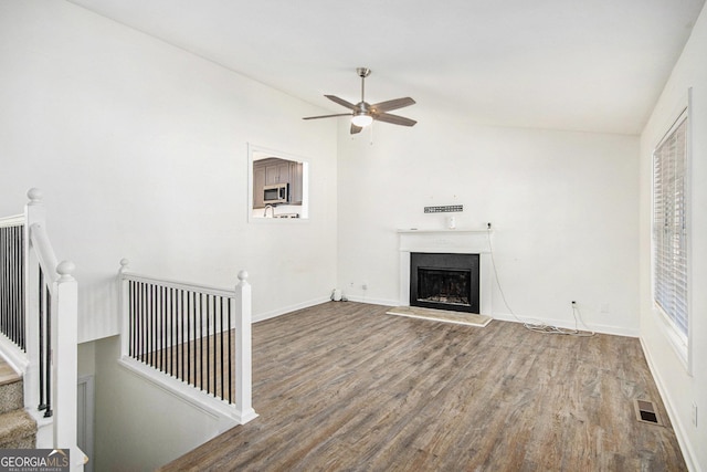 unfurnished living room featuring a fireplace with raised hearth, ceiling fan, wood finished floors, stairs, and vaulted ceiling