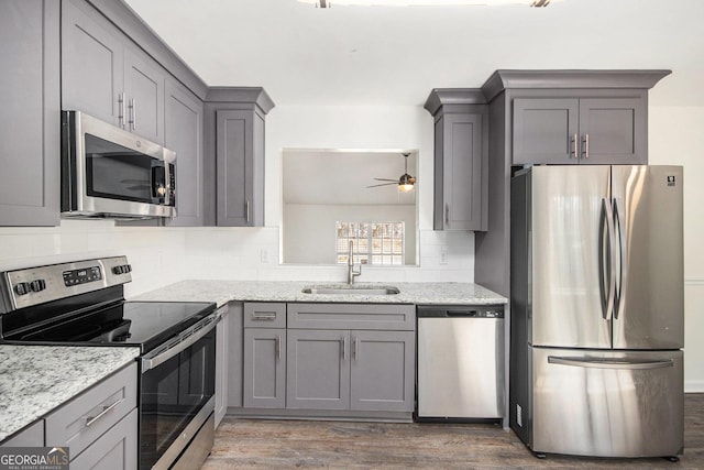 kitchen featuring light stone counters, stainless steel appliances, dark wood-style flooring, a sink, and gray cabinets