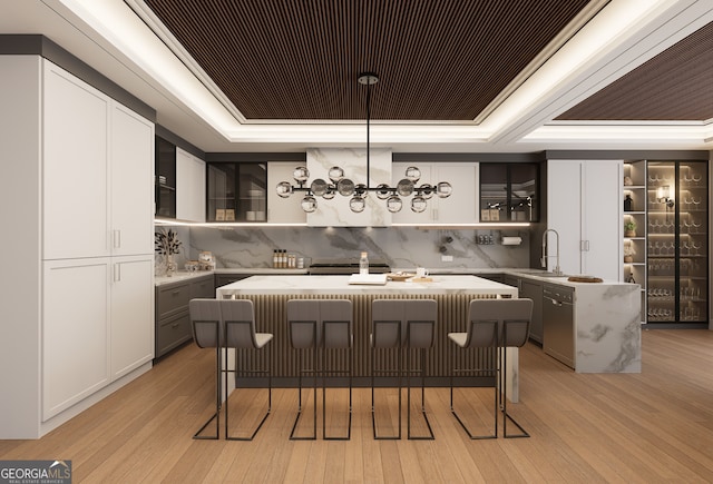 bar with tasteful backsplash, gray cabinetry, light hardwood / wood-style floors, and a tray ceiling