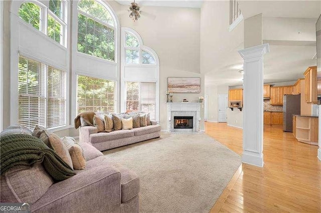 living room featuring decorative columns, a towering ceiling, and light wood-type flooring