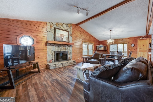 living room featuring wood-type flooring, a stone fireplace, vaulted ceiling with beams, and a textured ceiling