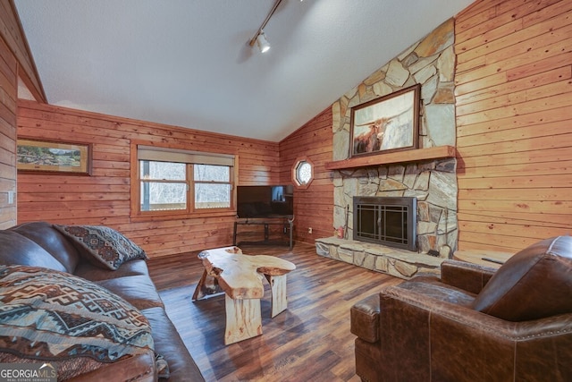 living room with wooden walls, a stone fireplace, vaulted ceiling, and hardwood / wood-style floors