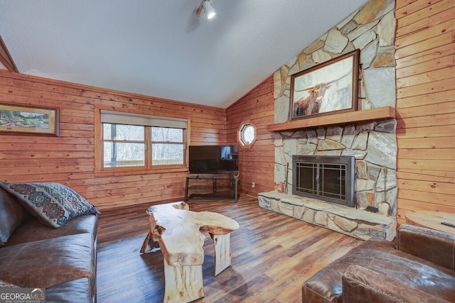 living room featuring vaulted ceiling, a stone fireplace, wooden walls, hardwood / wood-style flooring, and a textured ceiling