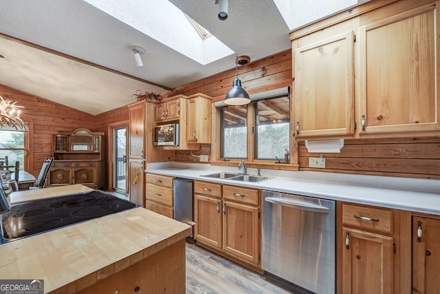 kitchen featuring lofted ceiling with skylight, appliances with stainless steel finishes, wood walls, sink, and a textured ceiling