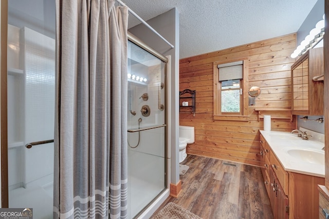 bathroom with toilet, an enclosed shower, wood walls, a textured ceiling, and hardwood / wood-style floors