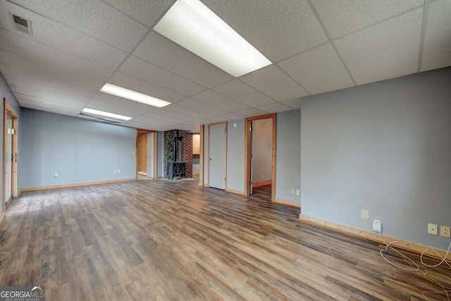 basement with hardwood / wood-style flooring, a paneled ceiling, and a wood stove
