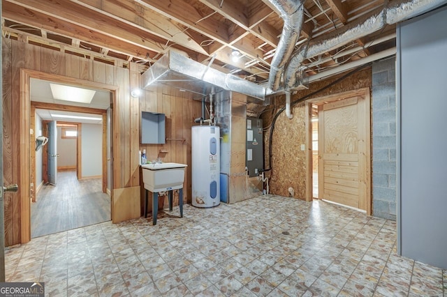 basement featuring heating unit, sink, electric water heater, and wood walls