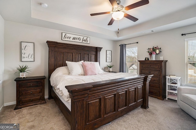 bedroom with multiple windows, a tray ceiling, light colored carpet, and visible vents