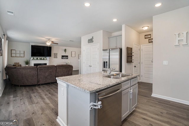 kitchen featuring a sink, open floor plan, a center island with sink, stainless steel appliances, and a fireplace