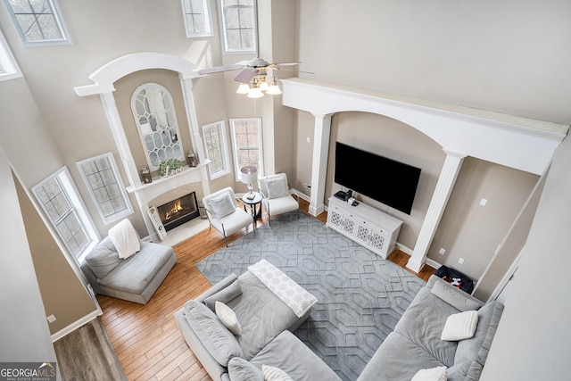 living room featuring a healthy amount of sunlight, a lit fireplace, a high ceiling, and wood finished floors